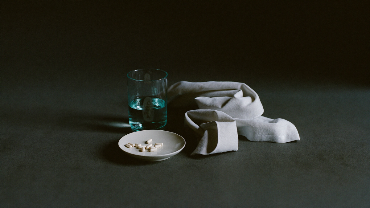 White dish of magnesium glycinate capsules beside a glass of water and folded linen on a dark surface
